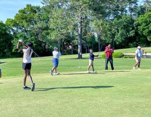 Black students practice their golf swings on a rolling green field