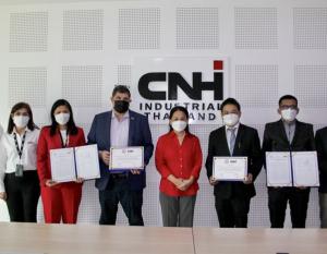 Group of people, all wearing protective masks, stand in front of CNHI sign in a conference room. Some hold documents