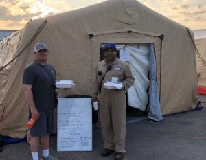 two people holding Styrofoam boxes and drinks outside a cloth tent