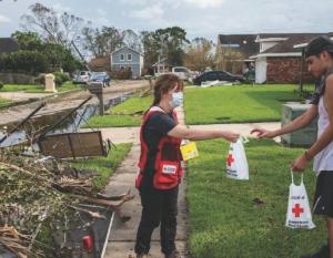 an american red cross volunteer handing a bag to another person, debris on the ground
