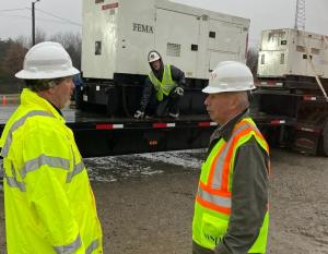 two workers outside stand beside a large trailer where two others are standing near a large generator on the trailer