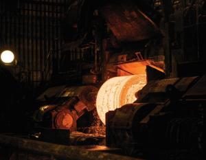 Large steel coil being formed just out of the furnace glows in a dark foundry