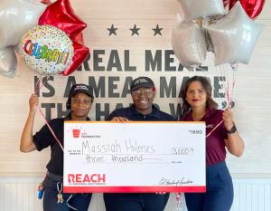 3 people hold a big check and balloons together 