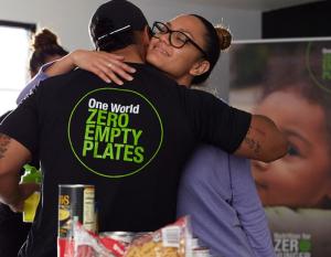 A person hugging someone with a t-shirt that reads: "One World, Zero Empty Plates"
