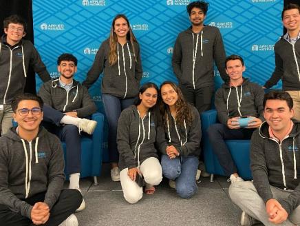 interns in gray hoodies pose in front of a blue applied materials logo wall