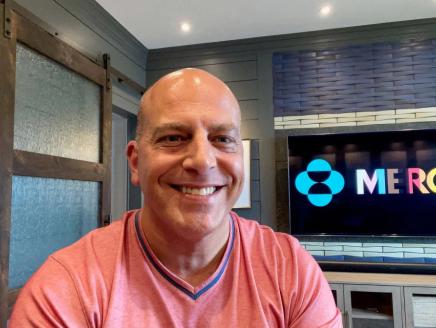 scott wright with a screen behind him playing the Merck logo in LGBTQ+ colors
