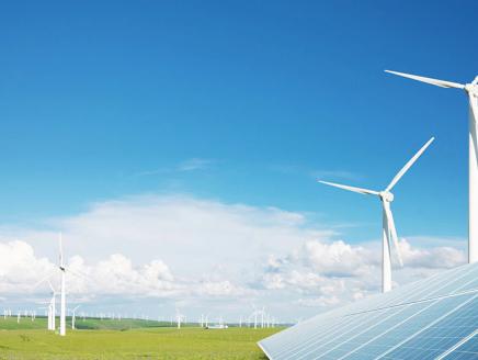 Outside on a bright day, windmills scattered on a large flat plain of grass, a solar panel in the right corner