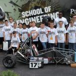 Large group of children stand behind a go-cart type vehicle. All wearing the same School of Engineering t-shirts