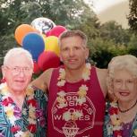 Henry Rodrique and his parents outside, wearing colorful leis, balloons behind them