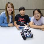 3 people sitting at a table with remote controlled robot