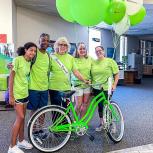Mary Lou Schlueter and family pose in green t-shirts behind a green bike and balloons