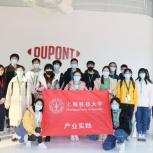 a group of people standing in front of a DuPont logo on a wall, holding a red sign with writing in a foreign language