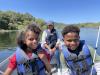 Danielle with her two children sitting in front of her in a boat on the water. All are wearing life vests.