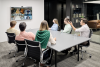 employees seated around a confrence table viewing other team members on a monitor mounted on a wall 