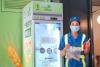 worker stands with a bag of food in front of a food bank refridgerator